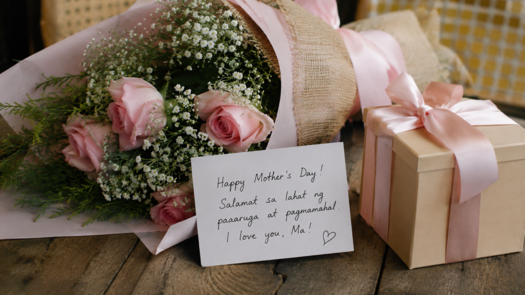 A bouquet of pink flowers, a handwritten Mother’s Day note in Filipino, and a wrapped gift displayed on a rustic wooden table in a warm Pampanga-inspired setting.
