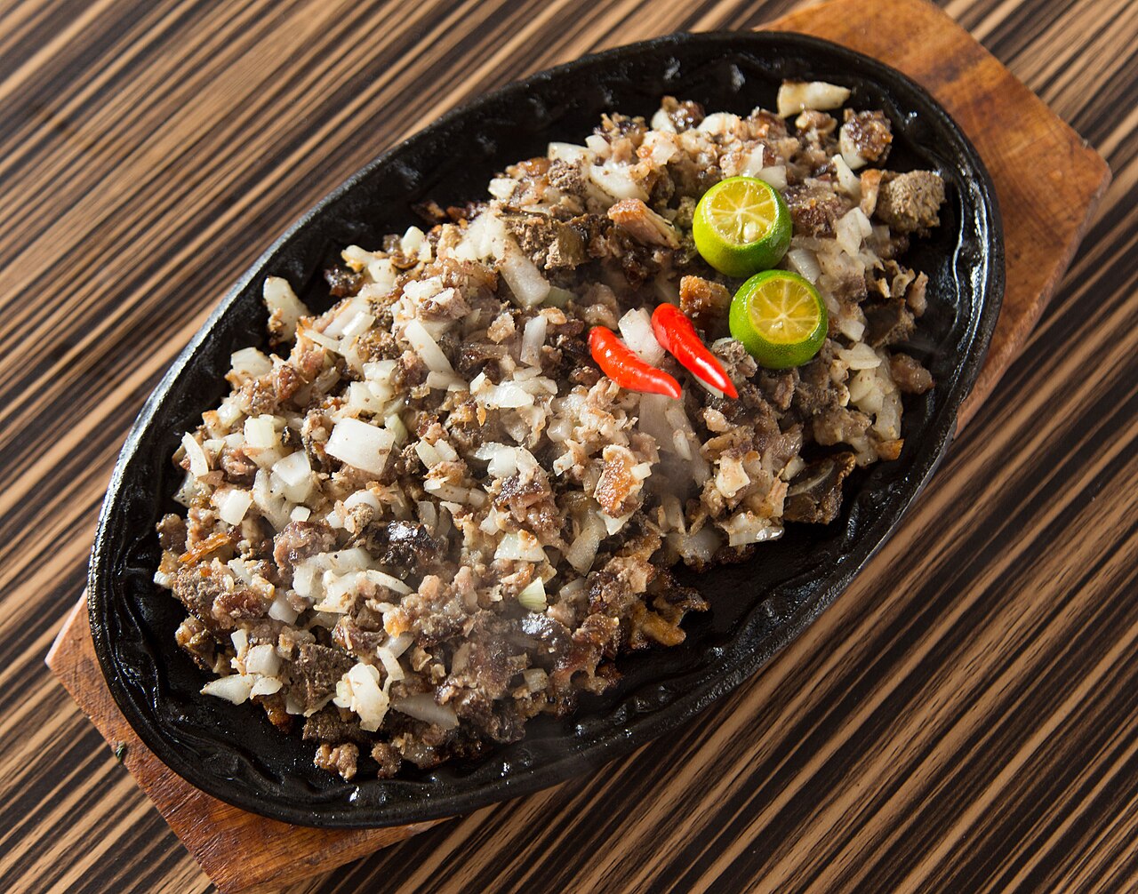 Traditional Kapampangan sisig served on a sizzling cast iron plate with calamansi and chili in Angeles City, Pampanga